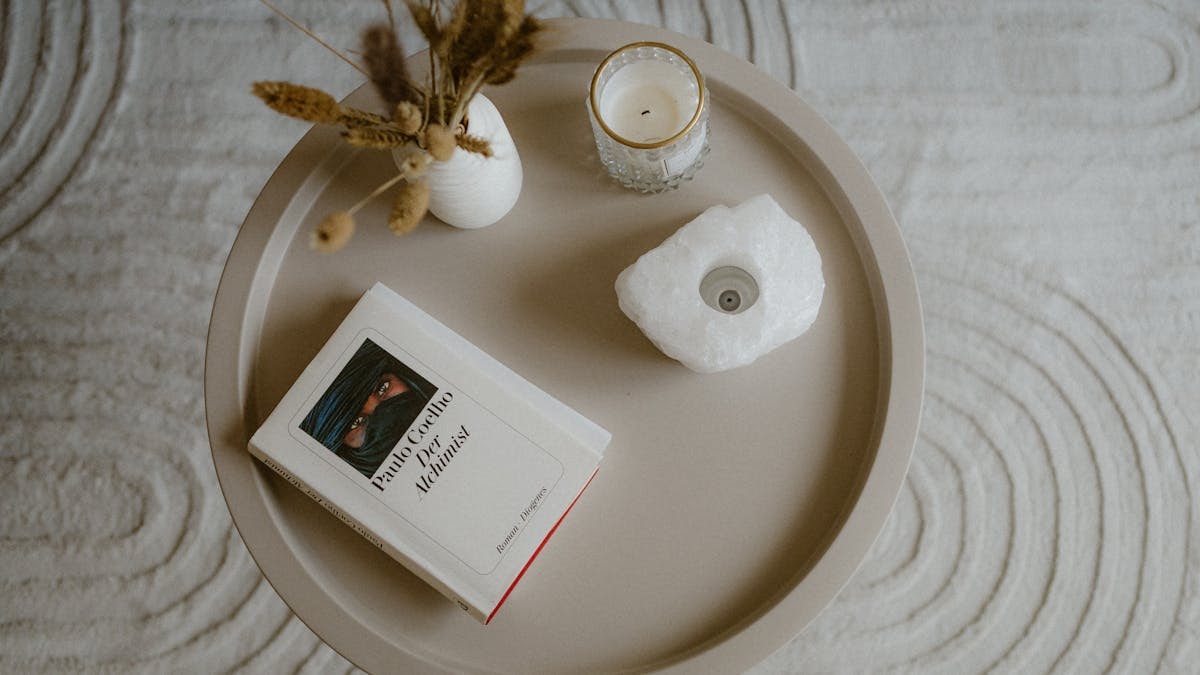 A cozy setup features a book, candle, and dried plants on a stylish coffee table.